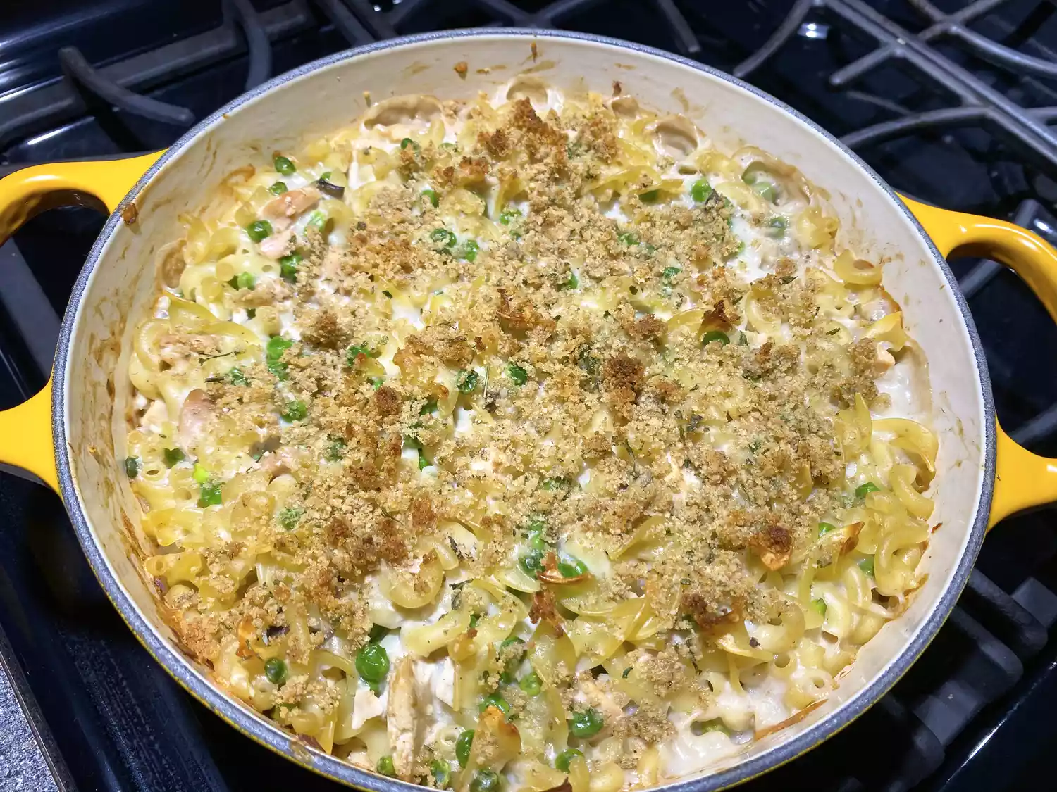 Finished dish 'Casserole' laid out in a yellow pan, presented with green peas, white sauce and breadcrumb seasoning.