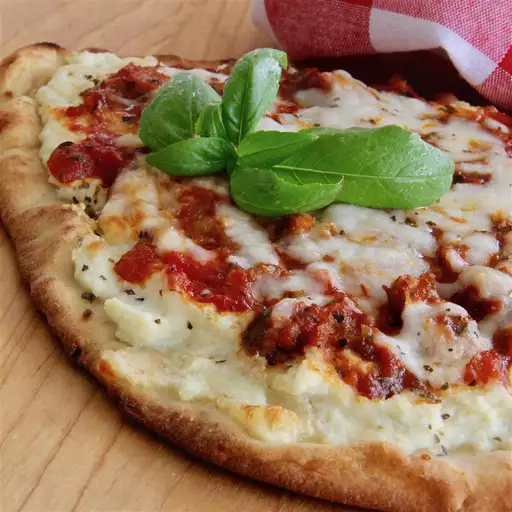 Finished dish 'Lasagna Flatbread', featuring a combination of red and white sauces, garnished with basil, atop a thin and crispy pizza bread.